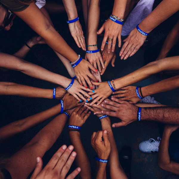 Group of people putting their hands in together standing in a circle wearing wrist blue bands