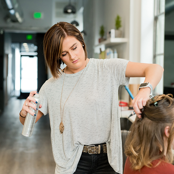 Young female stylist spraying a women's hair with hairspray product