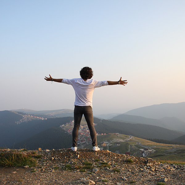 A man standing on the edge of cliff with his arms open