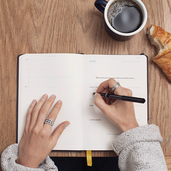 Woman writing in a notebook with a coffee and a croissant