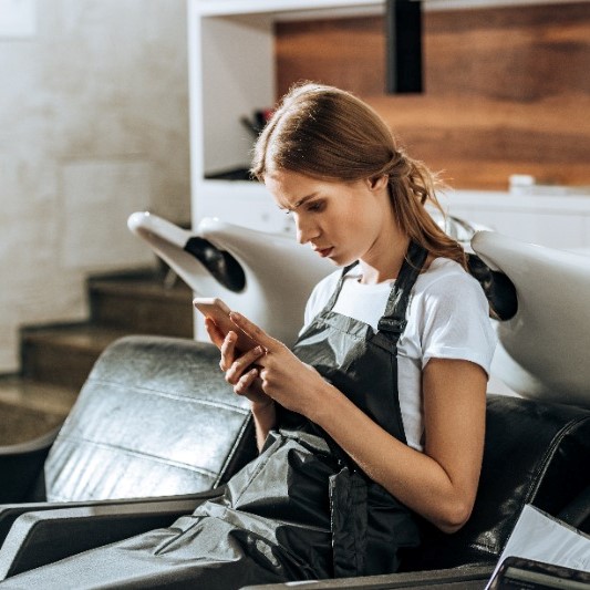 Image of woman waiting at a salon on her phone.